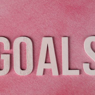 Motivational word 'GOALS' on a pink watercolor background for inspiration.